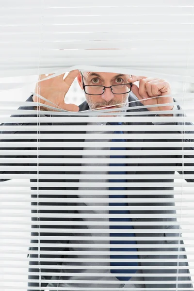 Retrato de um homem de negócios espreitando cortinas no escritório — Fotografia de Stock