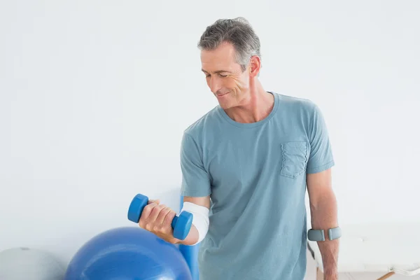 Smiling mature man with crutch and dumbbell — Stock Photo, Image