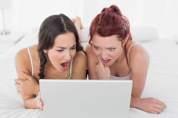 Shocked female friends looking at laptop in bed Royalty Free Stock Photos