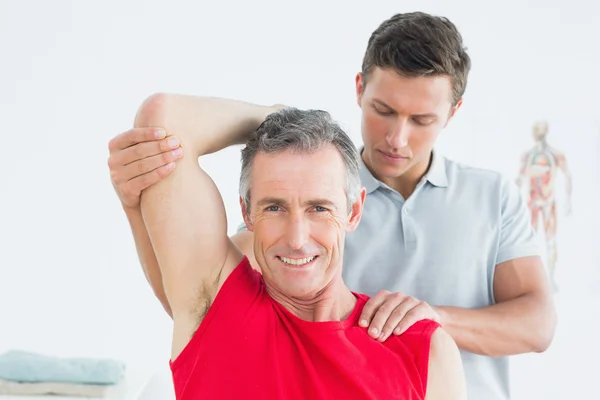 Physiotherapist stretching a smiling mature mans arm — Stock Photo, Image