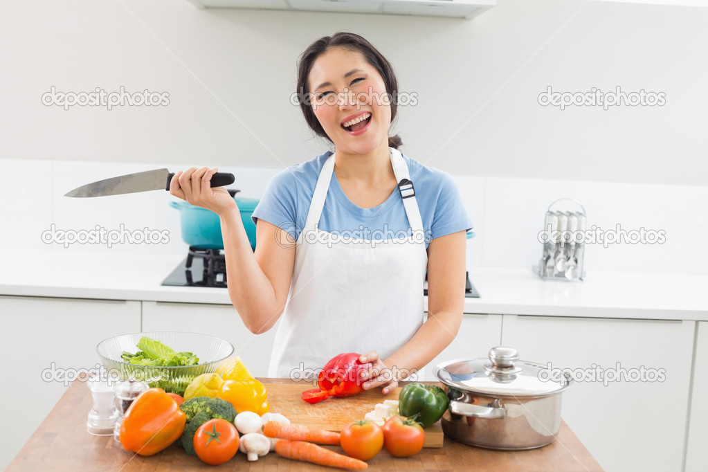 Thoughtful smiling woman chopping vegetables in kitchen