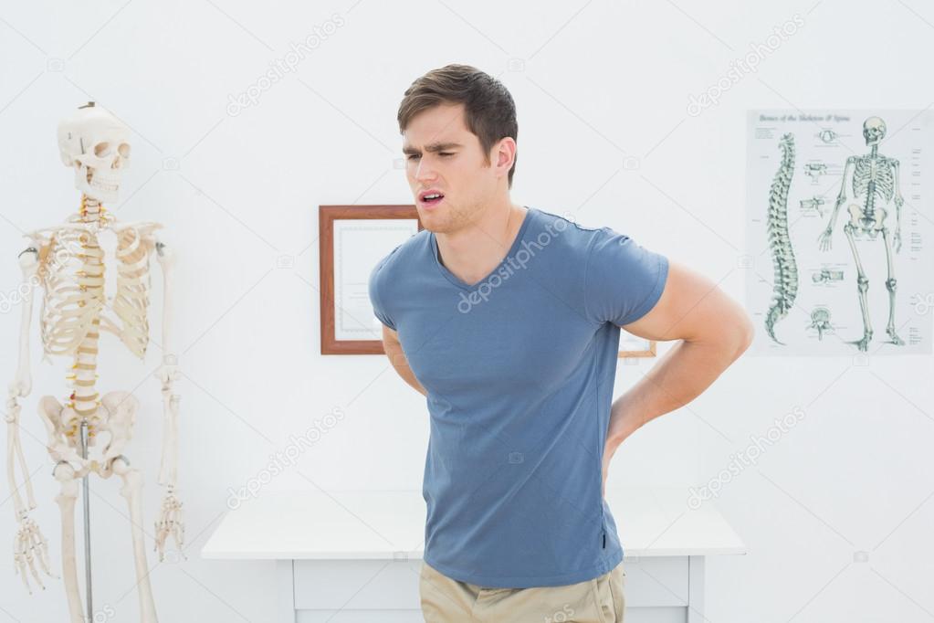 Handsome young man with back pain standing in office — Stock Photo