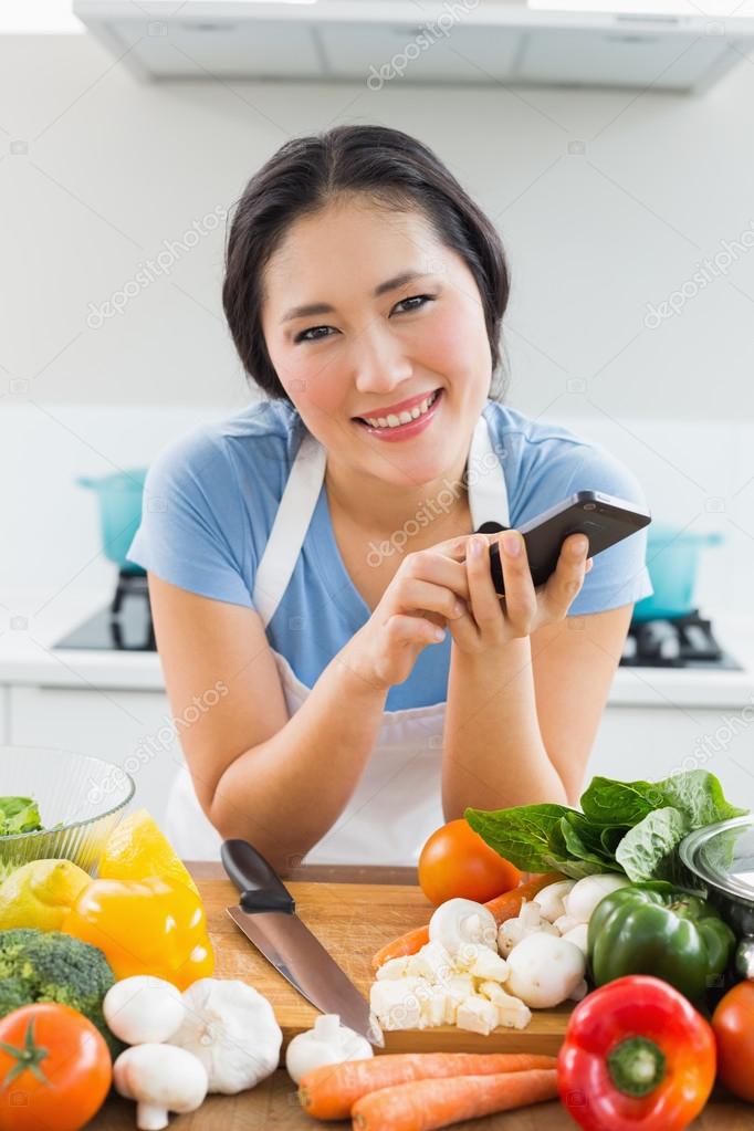 Smiling woman text messaging in front of vegetables in kitchen