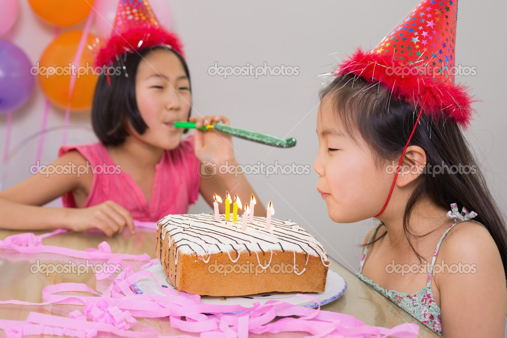 Girls blowing noisemaker and birthday candles — Stock Photo