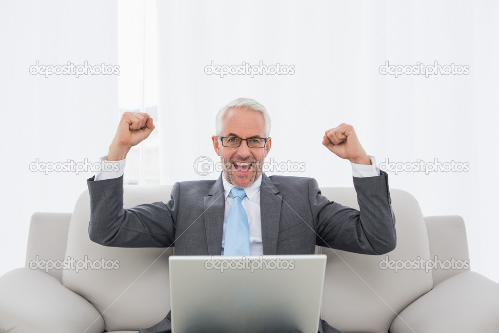 Elegant businessman cheering with laptop at home