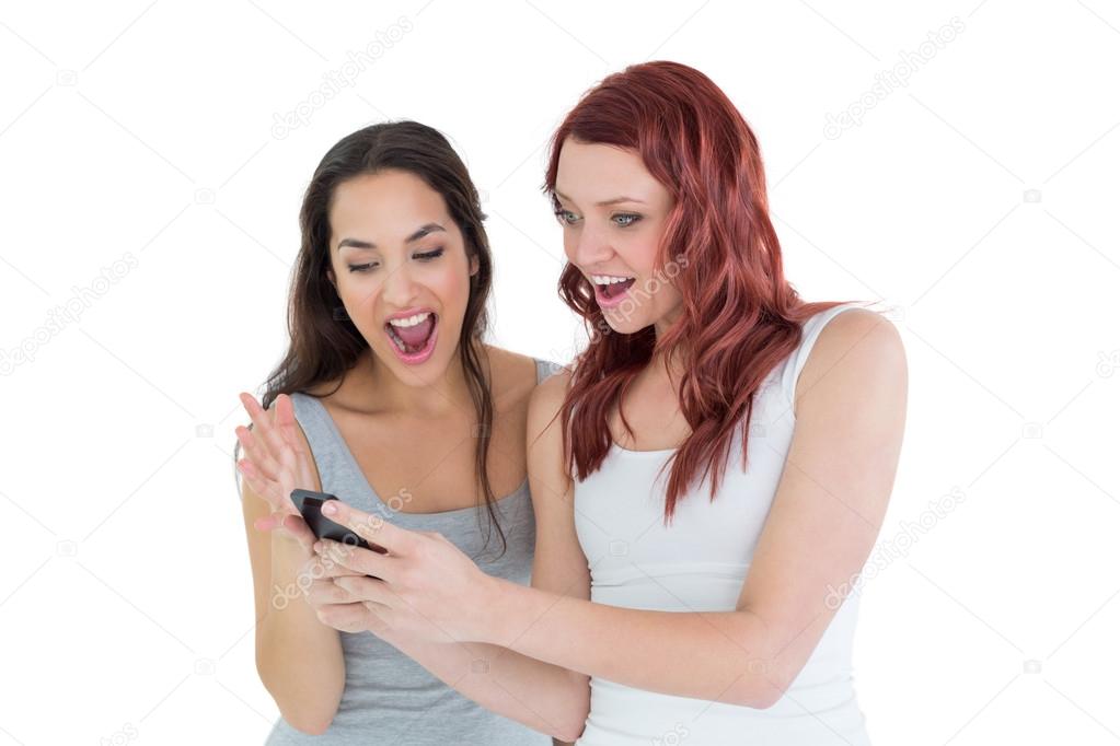 Shocked female friends looking at mobile phone