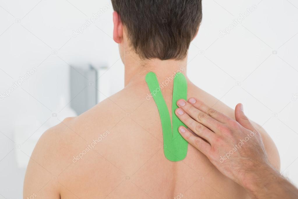 Rear view of a shirtless man with green kinesio tape on back