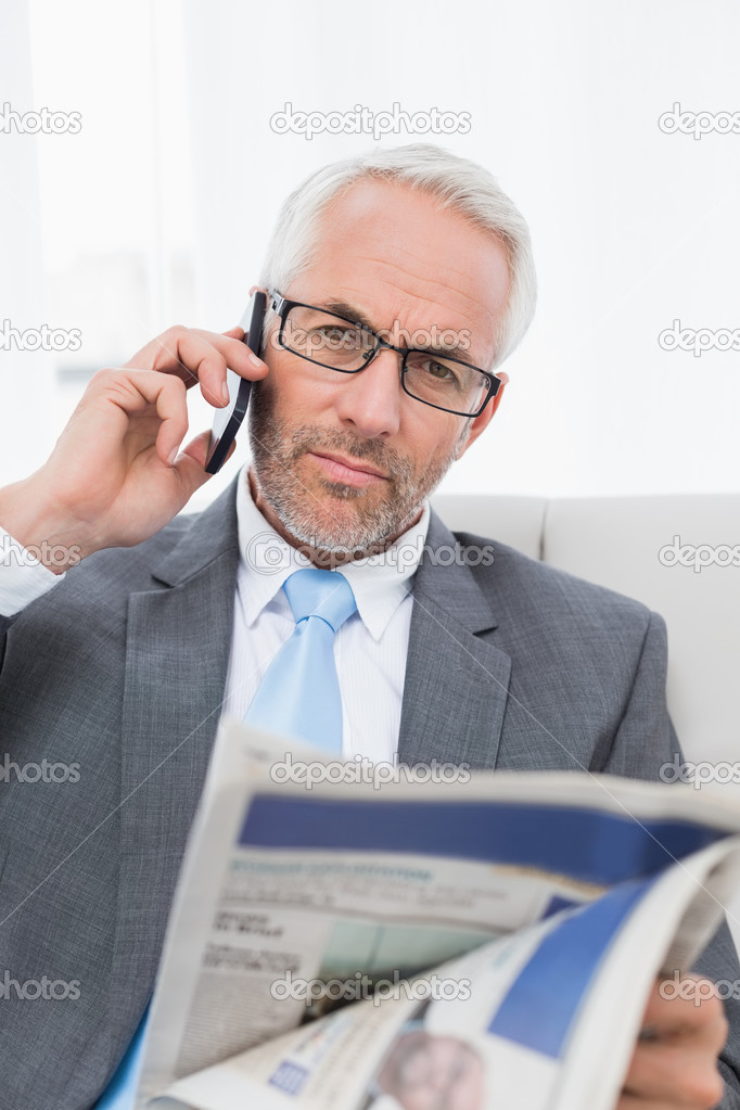 Serious businessman with cellphone and newspaper at home