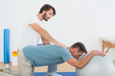 Fiziksel terapist yardımcı yoga topu ile genç adam