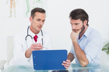 erkek doktor raporları hasta masada ile tartışıyor.