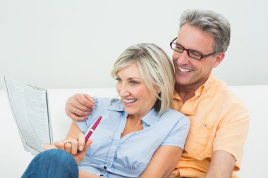 Happy couple doing the newspaper crossword puzzle at home clipart