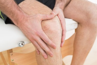 Mid section of a man with his hands on a painful knee clipart