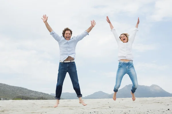 Cheerful young couple jumping at beach — Stock Photo, Image