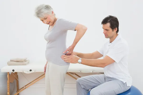 Fisioterapeuta masculino examinando la espalda de una mujer mayor — Foto de Stock