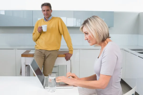 Mujer usando portátil y hombre con taza de café en la cocina —  Fotos de Stock