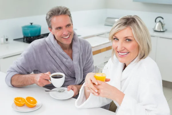 Pareja feliz en albornoces desayunando en la cocina —  Fotos de Stock