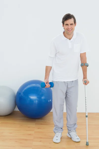 Portrait of a smiling man with crutch and dumbbell — Stock Photo, Image