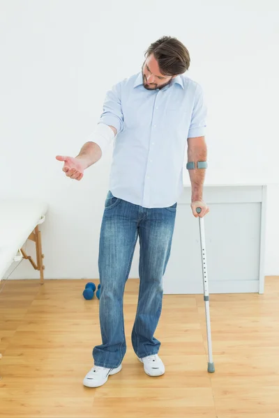 Young man with crutch and bandaged hand — Stock Photo, Image