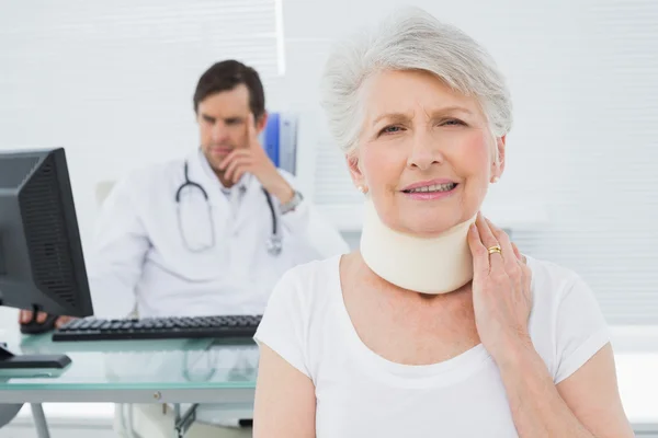 Senior patient in surgical collar with doctor in background at o — Stock Photo, Image