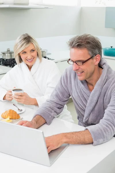 Paar in badjassen met laptop in de keuken — Stockfoto