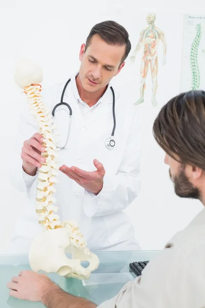 Médico masculino explicando a coluna vertebral a um paciente — Fotografia de Stock