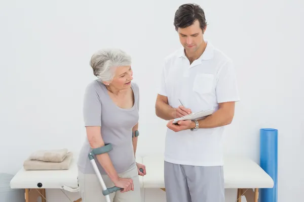 Terapeuta discutiendo informes con un paciente mayor discapacitado — Foto de Stock