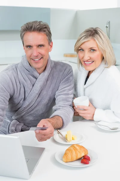Couple in bathrobes using laptop in kitchen — Stock Photo, Image