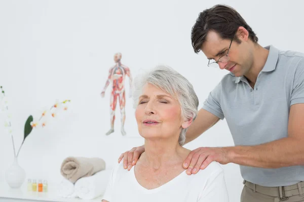 Fisioterapeuta masculino masajeando los hombros de una mujer mayor — Foto de Stock