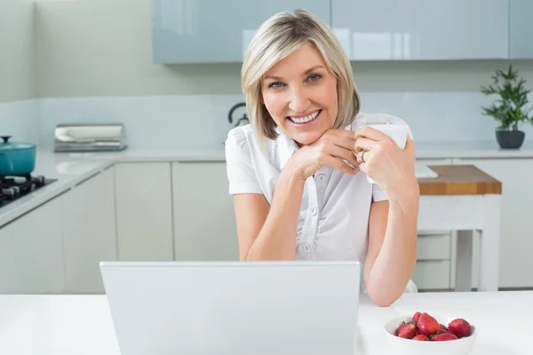 Mulher casual com xícara de café e laptop na cozinha — Fotografia de Stock