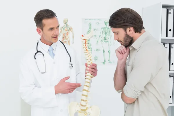 Médico masculino explicando a coluna vertebral a um paciente — Fotografia de Stock