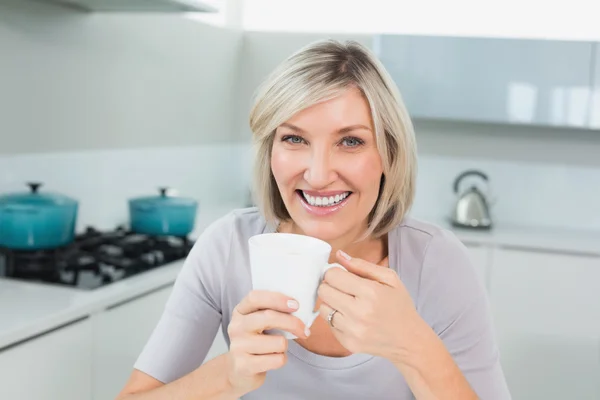 Smiling casual woman with coffee cup in kitchen — Stock Photo, Image