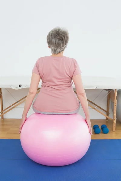 Vista trasera de una mujer mayor sentada en una pelota de yoga —  Fotos de Stock