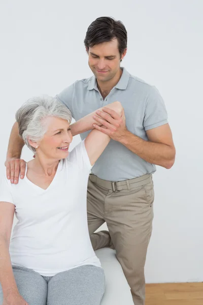 Fysiotherapeut uitrekken een senior lachende vrouw arm — Stockfoto