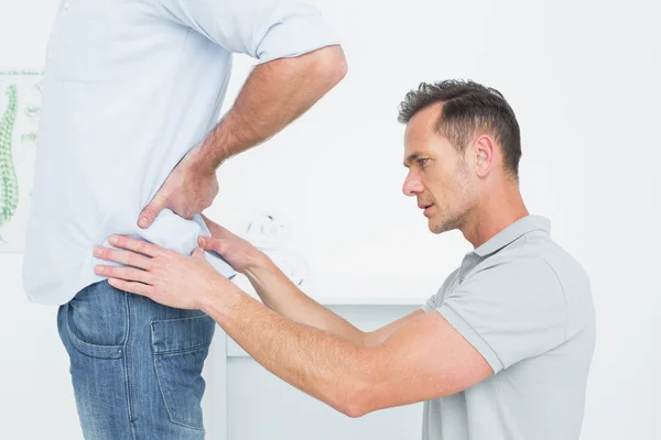 Vista lateral de un fisioterapeuta masculino examinando la espalda del hombre — Foto de Stock