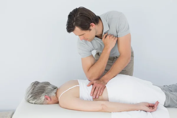 Fisioterapeuta masculino masajeando la espalda de una mujer mayor — Foto de Stock