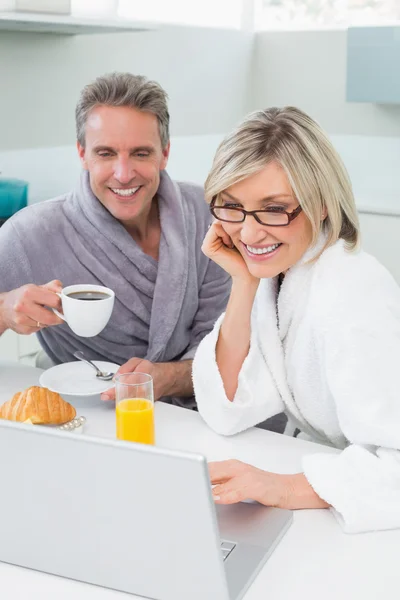 Couple in bathrobes with coffee and juice using laptop — Stock Photo, Image
