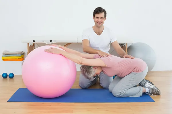 协助高级女子与瑜伽球的物理治疗师 — 图库照片