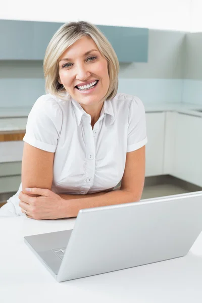 Mujer feliz casual con ordenador portátil en la cocina — Foto de Stock