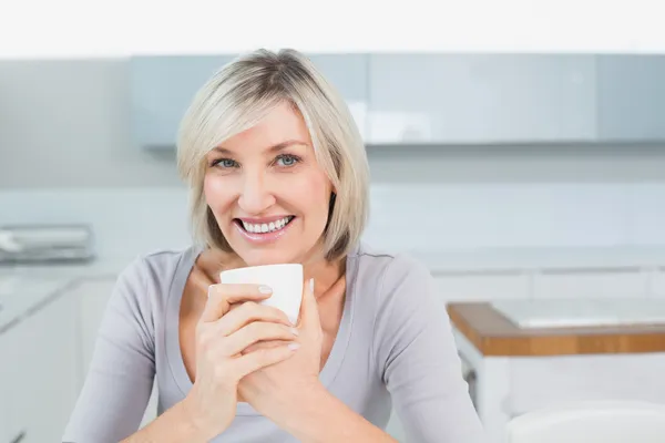 Lachende jonge vrouw met koffie beker in keuken thuis — Stockfoto