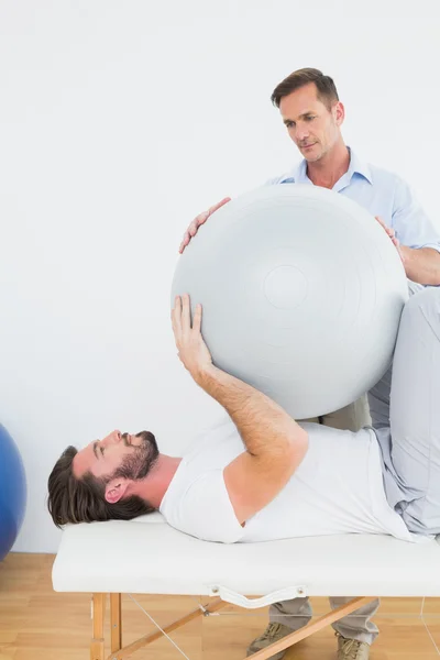 Fysieke therapeut helpen jonge man met yoga bal — Stockfoto