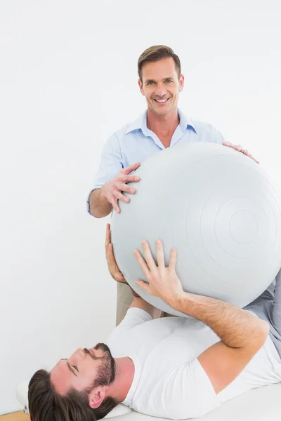 Physical therapist assisting young man with yoga ball — Stock Photo, Image