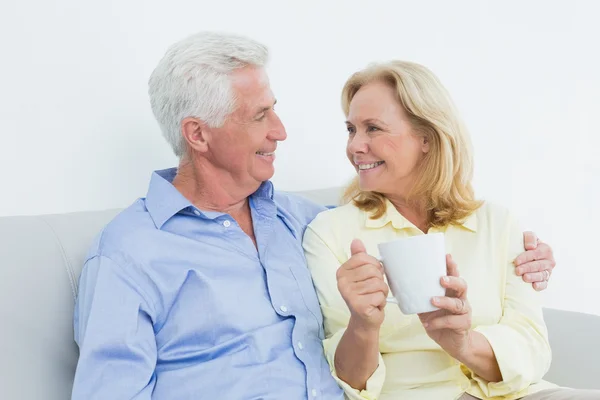 Starší pár s šálek kávy sedí na pohovce — Stock fotografie