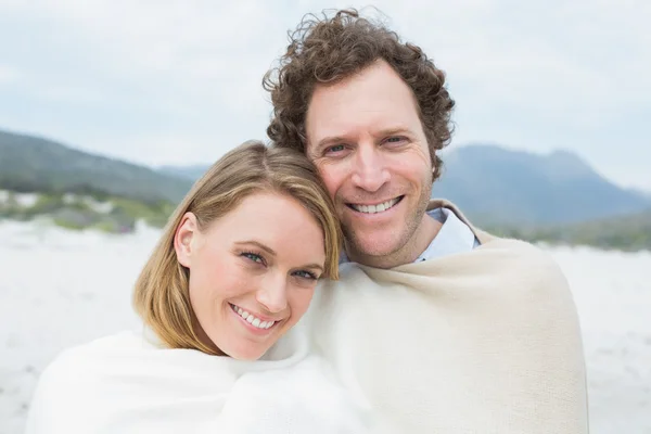 Smiling couple wrapped in blanket at beach — Stock Photo, Image