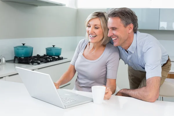 Happy couple using laptop in kitchen — Stock Photo, Image