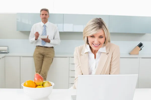 Vrouw met laptop en man op achtergrond in kitchen — Stockfoto