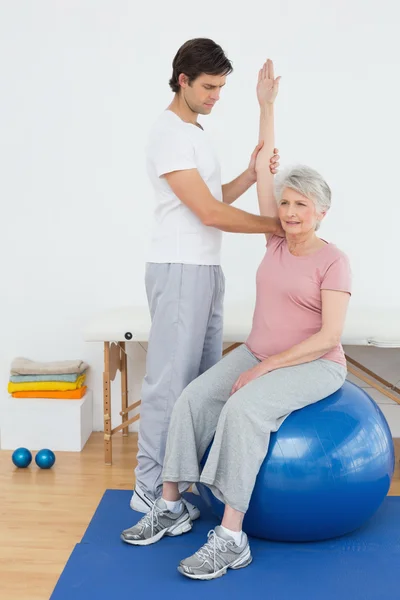 Donna anziana sulla palla di yoga con un fisioterapista — Foto Stock