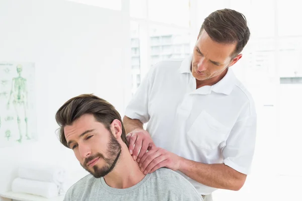 Terapeuta do sexo masculino massageando o pescoço de um jovem — Fotografia de Stock