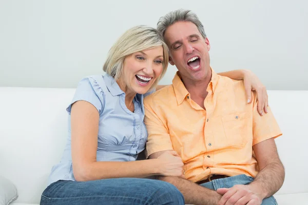 Cheerful couple sitting on sofa at home — Stock Photo, Image