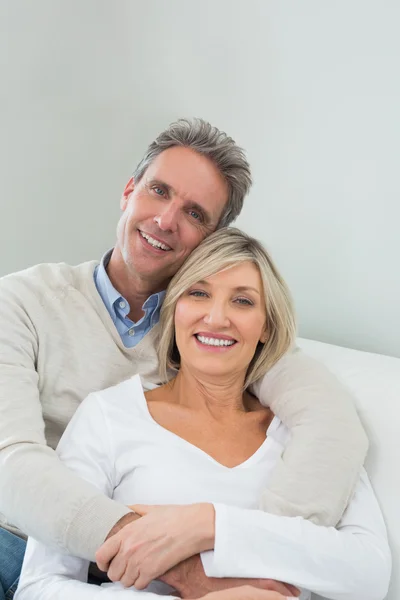 Glückliches Paar umarmt sich, während es zu Hause auf dem Sofa sitzt — Stockfoto