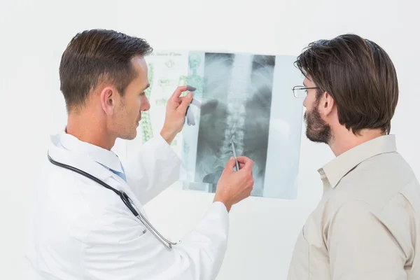 Médico masculino que explica a radiografia da coluna vertebral ao paciente — Fotografia de Stock